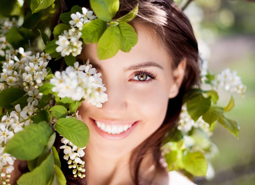 young woman smiling behind white flowers