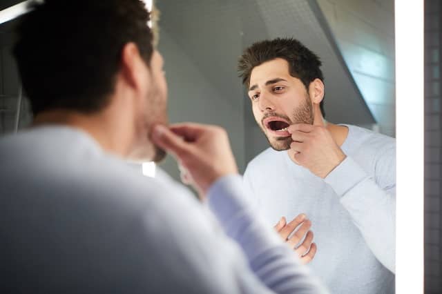 young man checking tooth in bathroom mirror