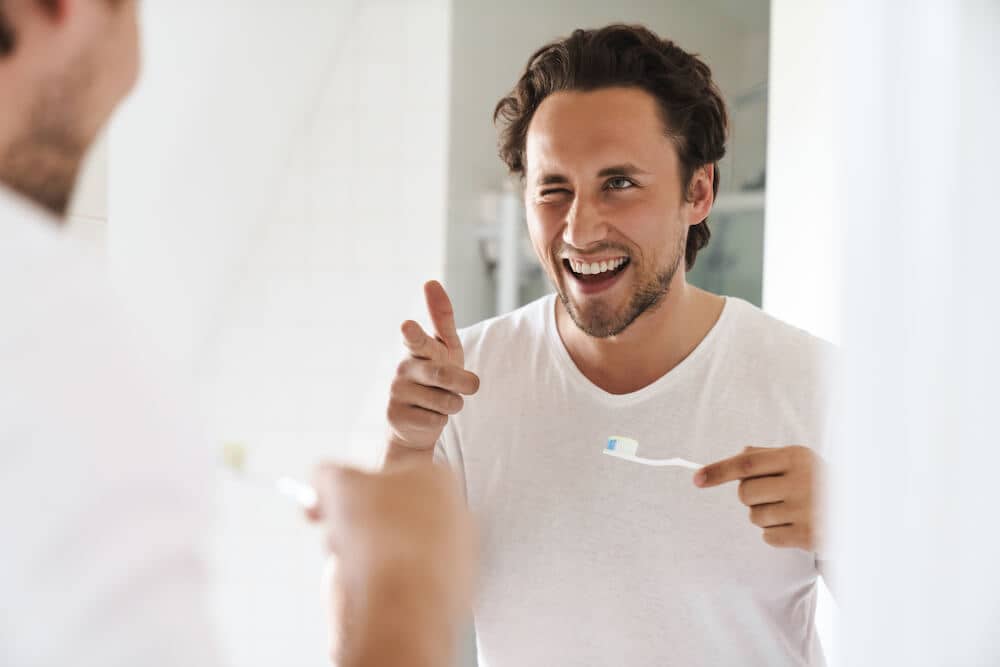man pointing at a mirror while holding a toothbrush