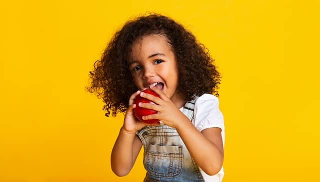 little girl biting red apple